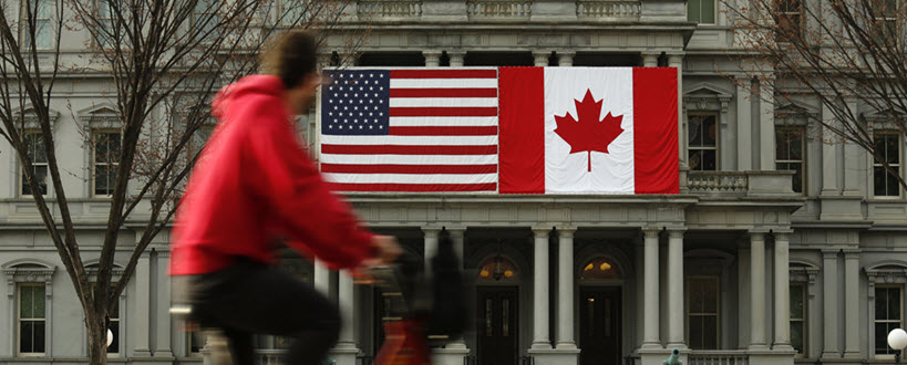 Un homme roulant à vélo avec les drapeaux du Canada et des États-Unis en arrière-plan.