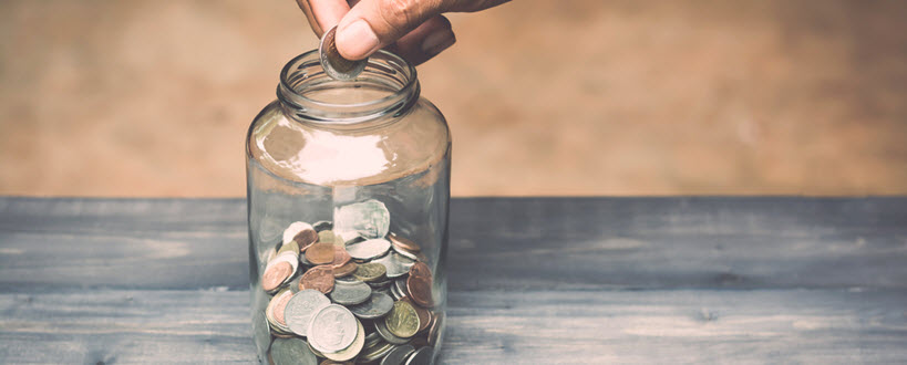 Gros plan d’une main d’homme déposant une pièce de monnaie dans un pot Mason.