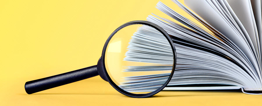Magnifying glass pointed at a book with its pages turning.