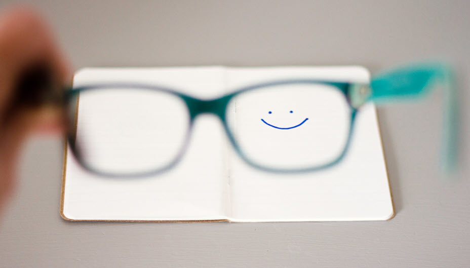Smiley face drawn on a notebook shown through a pair of eyeglasses.