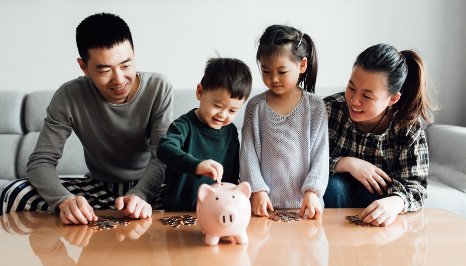 A family of four watching as the youngest puts coins into a piggy bank.
