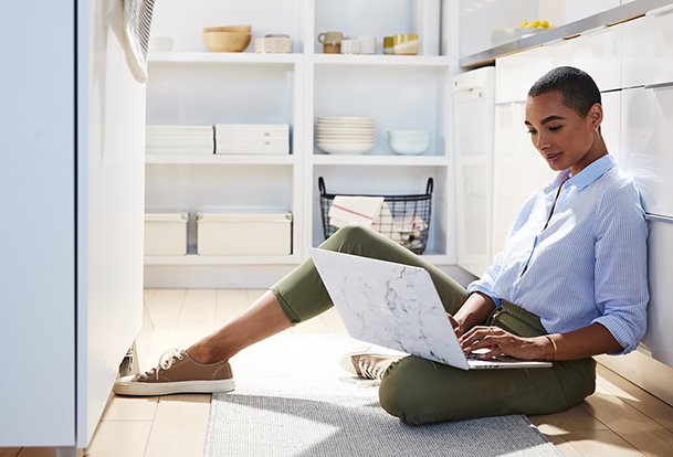 Femme assise sur le sol de la cuisine avec un ordinateur portable.