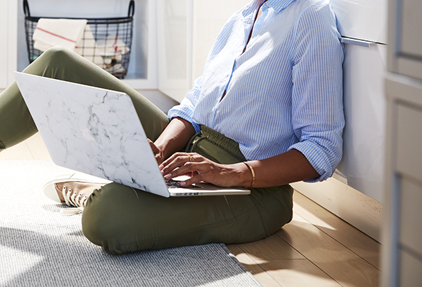 Femme travaillant sur un ordinateur portable, assise sur un plancher de cuisine.