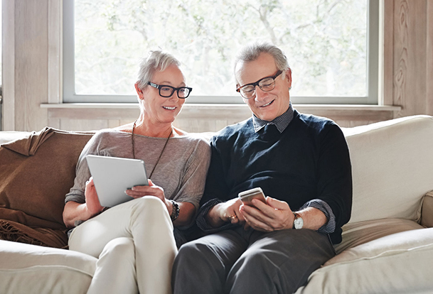 Une femme et un homme assis sur un divan, des gadgets dans les mains.