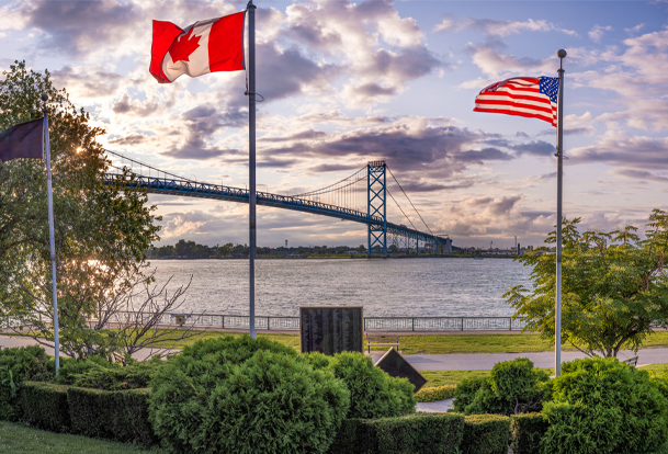 Canadian and U.S. flags in the foreground with a bridge in the background.