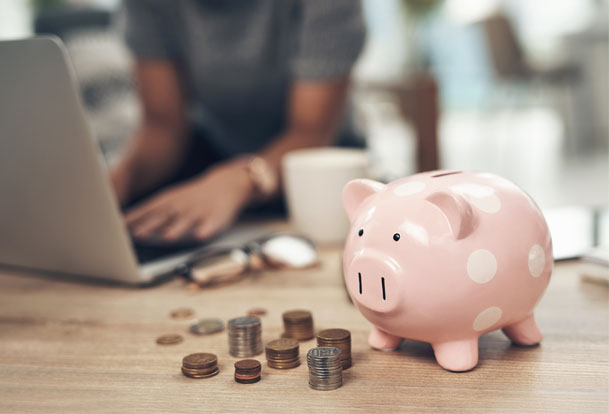 Piggy bank and coins in the foreground, and a person working at their home office in the background.