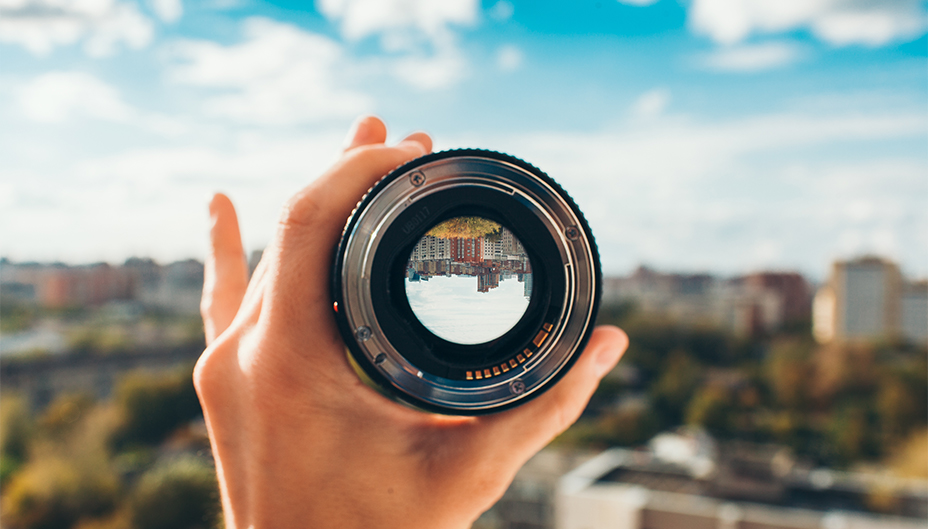 A person holds a camera lens to a city skyline in a concept for income projection.