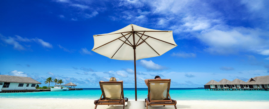 Two people lounging under an umbrella on the beach.
