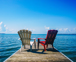 Two muskoka chairs on a dock.